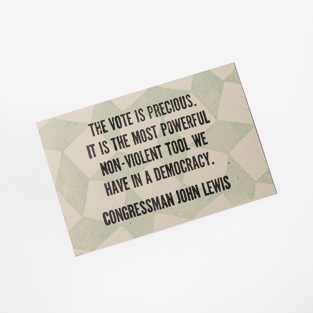 The John Lewis Quote Postcard is hand-printed with the phrase, "The vote is precious. It is the most powerful non-violent tool we have in a democracy," and features a beige and green geometric background crafted by Liberty Craftworks.