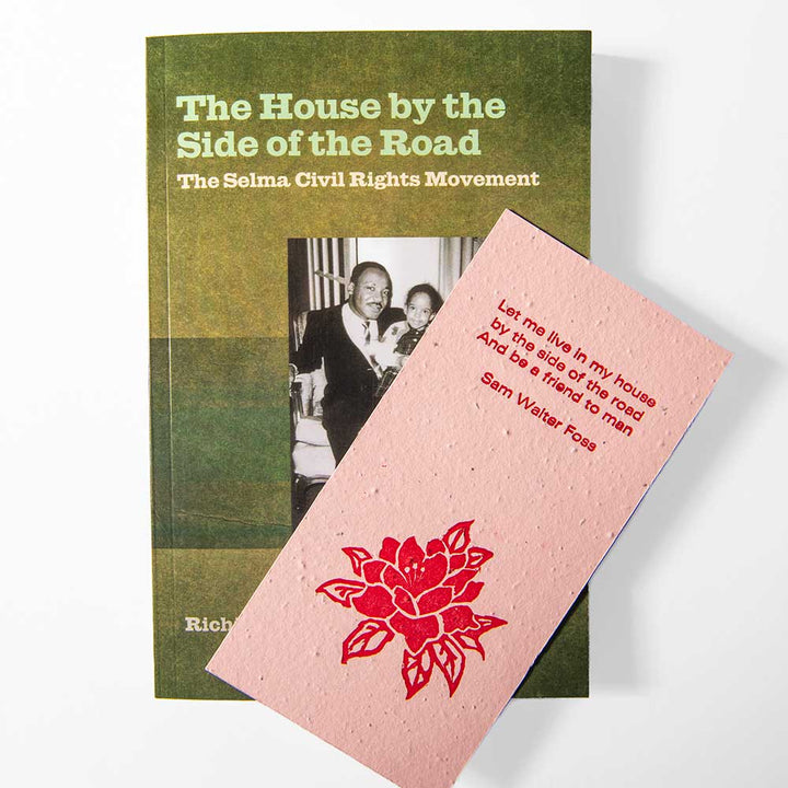 The House by the Side of the Road Bookmark is displayed on a white background, overlapping with a pink card featuring a red rose illustration and an inspirational excerpt from a Sam Walter Foss poem, alongside the book "The Selma Civil Rights Movement." The bookmark is handcrafted from seeded paper.