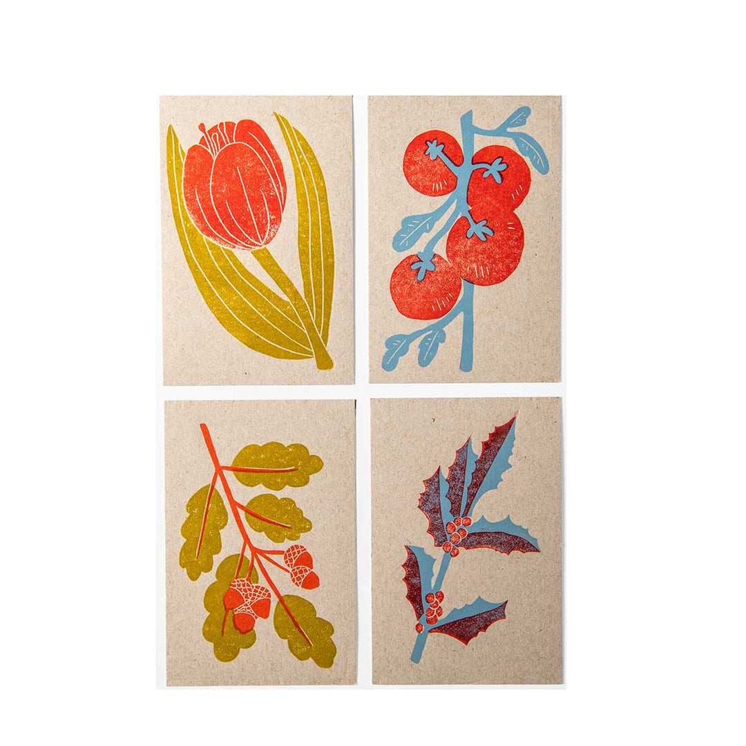 The Four Seasons Postcard Set features four illustrated cards—tulip, tomato vine, oak with acorns, and holly with berries—in vibrant colors on kraft paper, creating a nature-inspired handmade postcard collection.
