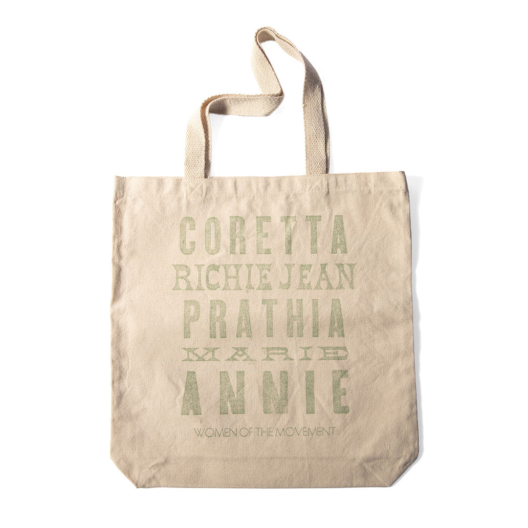 The Women of the Movement Tote is a beige, handcrafted bag made from durable cotton canvas. It features the names CORETTA, RICHIE JEAN, PRATHIA, MARIE, and ANNIE in green text above the phrase "WOMEN OF THE MOVEMENT," serving as a tribute to influential women of the Civil Rights Movement.