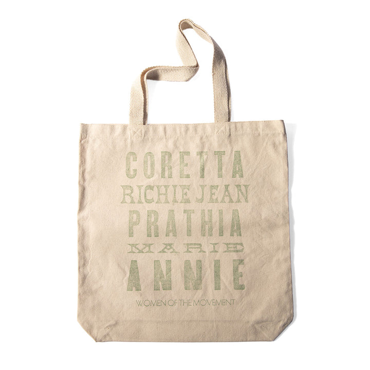 The Women of the Movement Tote is a beige, handcrafted bag made from durable cotton canvas. It features the names CORETTA, RICHIE JEAN, PRATHIA, MARIE, and ANNIE in green text above the phrase "WOMEN OF THE MOVEMENT," serving as a tribute to influential women of the Civil Rights Movement.