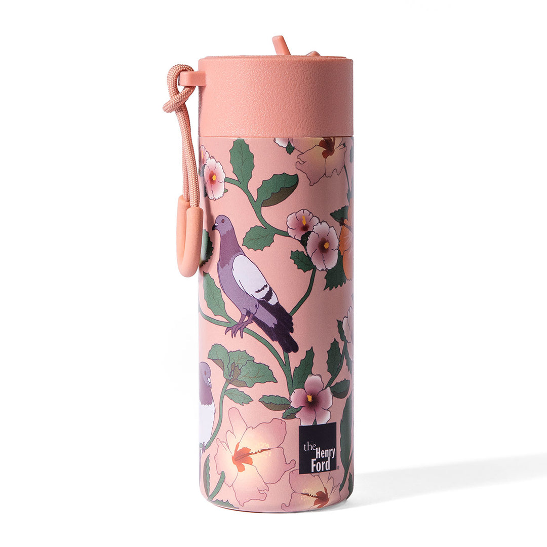 The Roberto Lugo Pigeon Art Water Bottle is a pink travel tumbler adorned with a floral and bird pattern, featuring a matching pink lid with a looped strap and The Henry Ford logo near the bottom. This insulated stainless steel bottle combines style and functionality for your daily adventures.