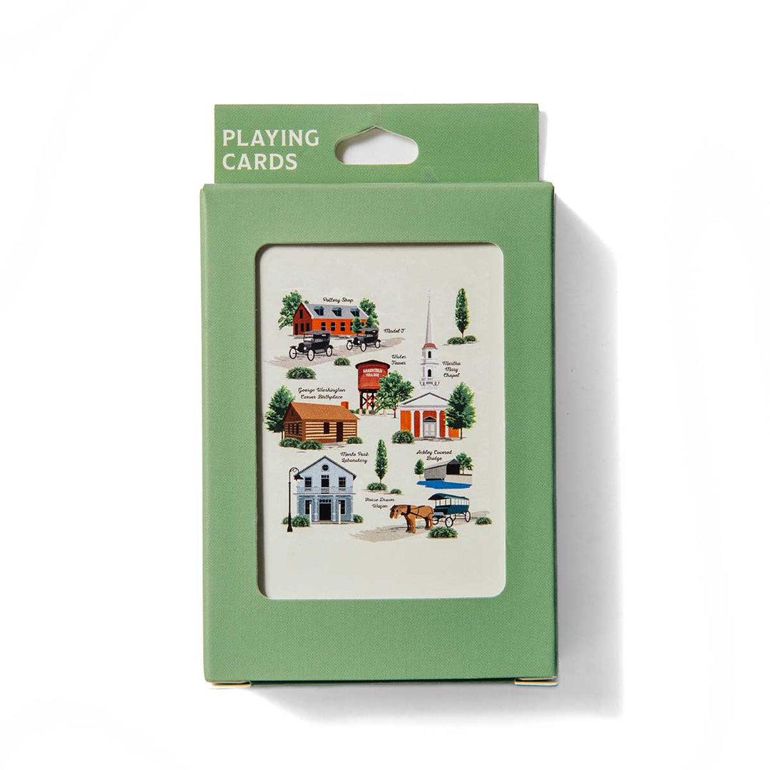 A green box of Greenfield Village Playing Cards features illustrations of various small town buildings and trees visible through a window on the front. This set provides an educational card game experience, bringing history to life with its charming artwork.