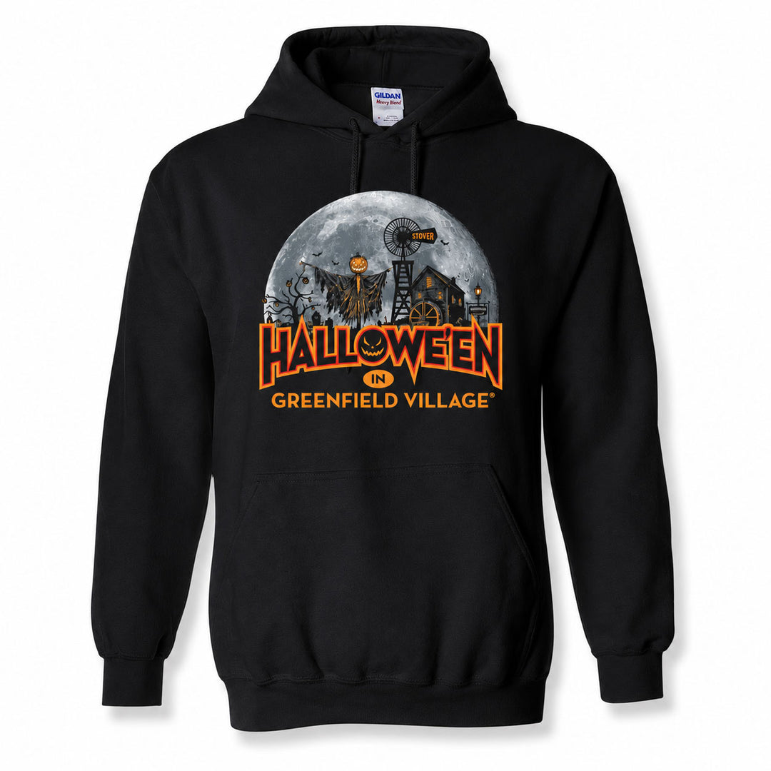 The Henry Ford® Greenfield Village Halloween Glow Hooded Sweatshirt is a black glow-in-the-dark hoodie featuring a festive Halloween design with a full moon, haunted house, pumpkins, and “Halloween in Greenfield Village” printed in bold orange letters on the front.