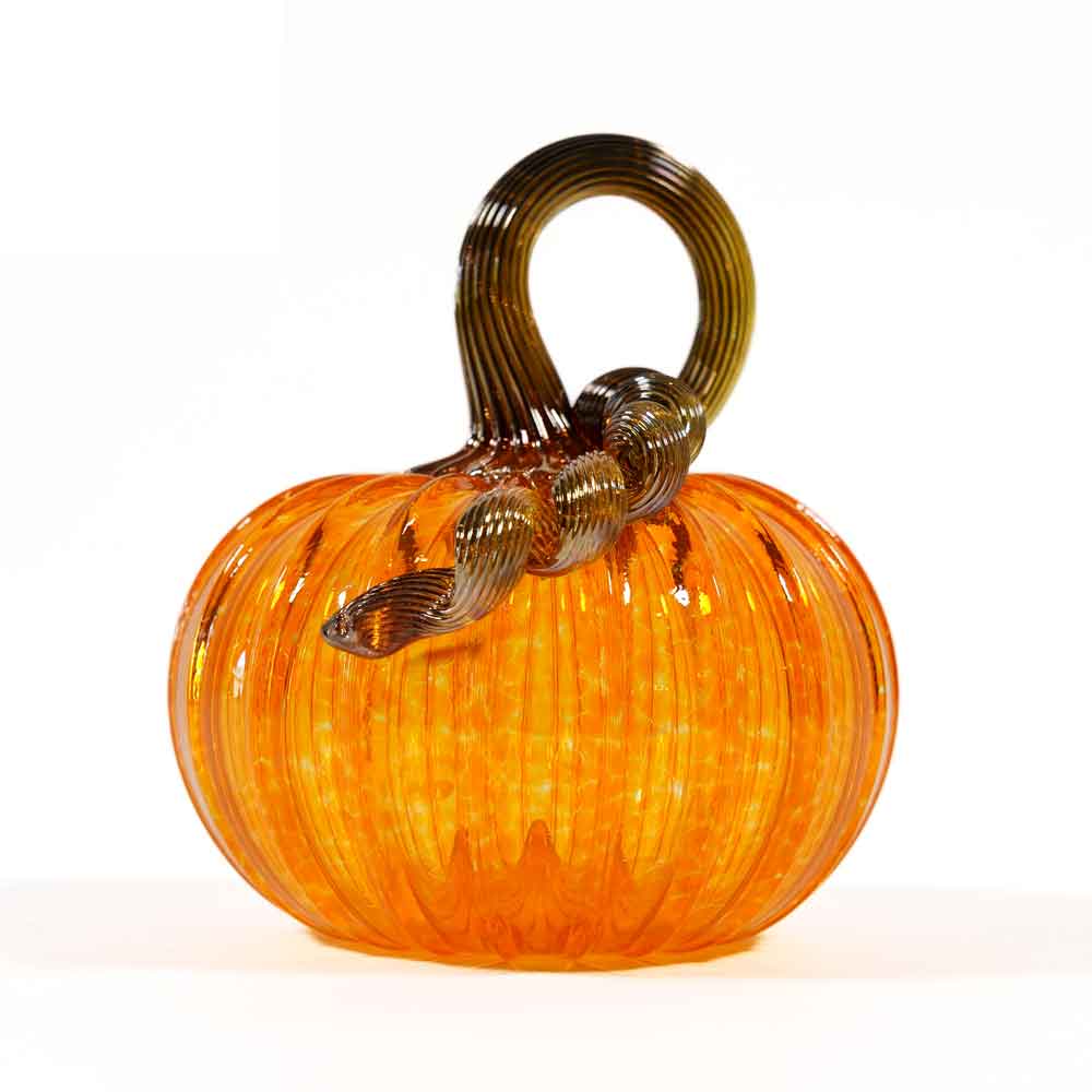 The Small Glass Pumpkin - Saffron features a vibrant orange hue with a ribbed texture and a twisted, dark green glass stem. Expertly hand blown for exquisite detail and charm, this collectible keepsake is displayed against a plain white background.