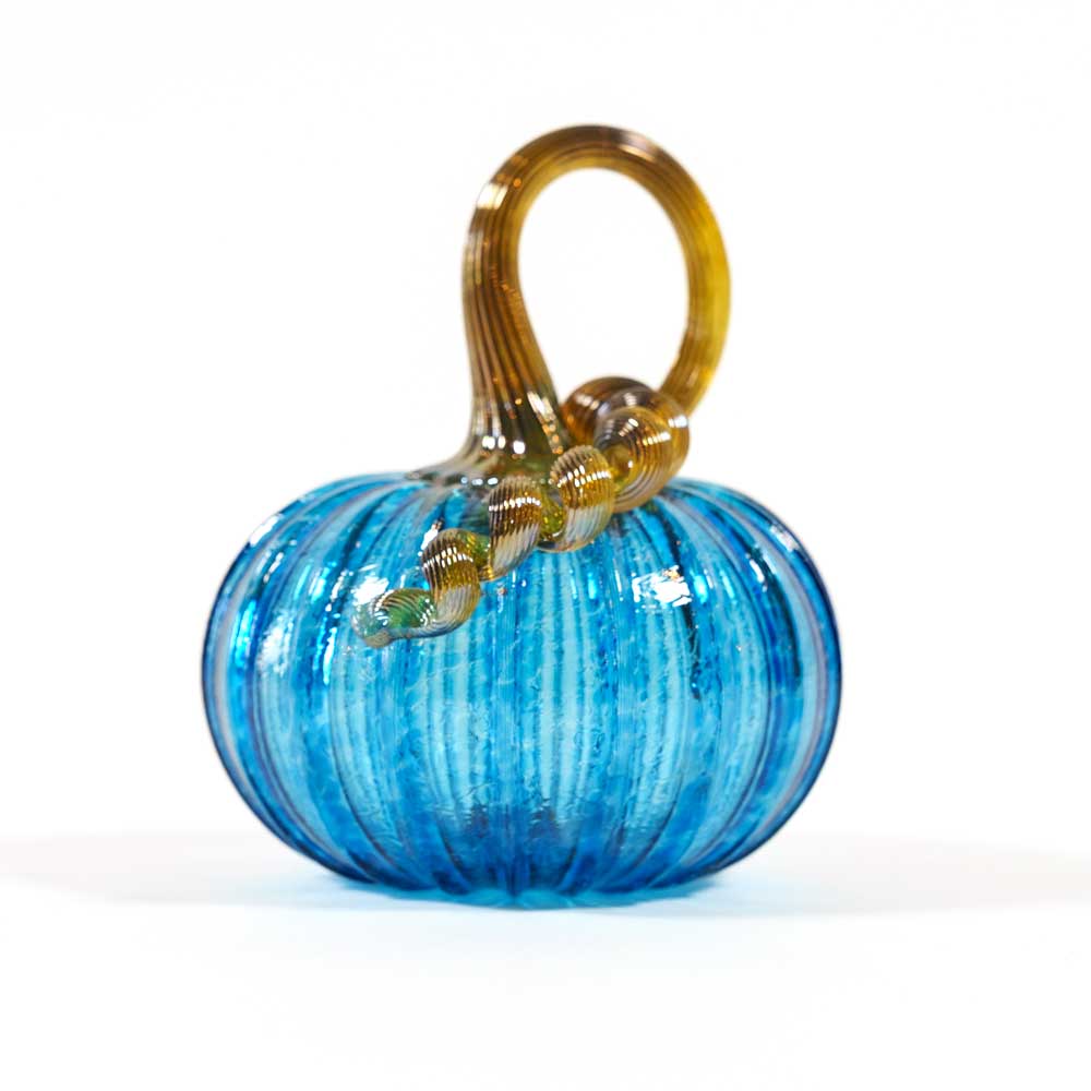 The Small Glass Pumpkin - Aqua is a hand-blown collectible featuring a vibrant aqua body with vertical ridges and a curled, translucent golden stem, inspired by Greenfield Village artistry. Set against a plain white background.