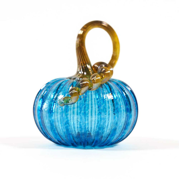The Small Glass Pumpkin - Aqua is a hand-blown collectible featuring a vibrant aqua body with vertical ridges and a curled, translucent golden stem, inspired by Greenfield Village artistry. Set against a plain white background.