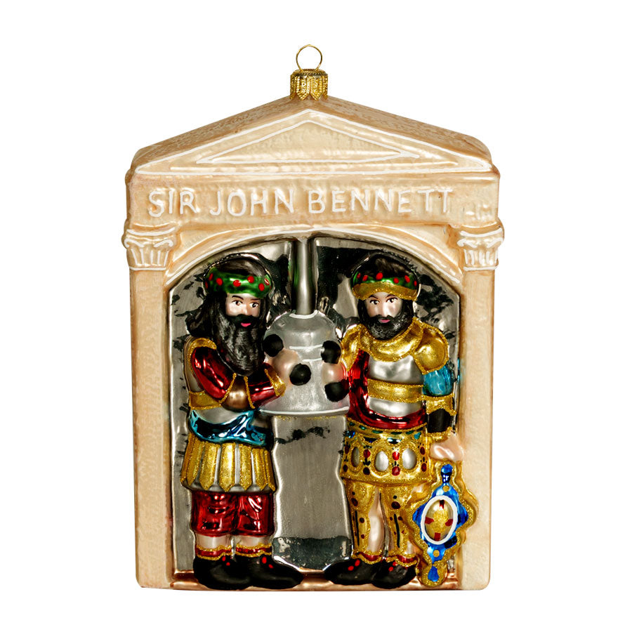The Sir John Bennett Ornament is a glass decoration shaped like a small building, with two colorful medieval figures beside a clock inside an arched opening.