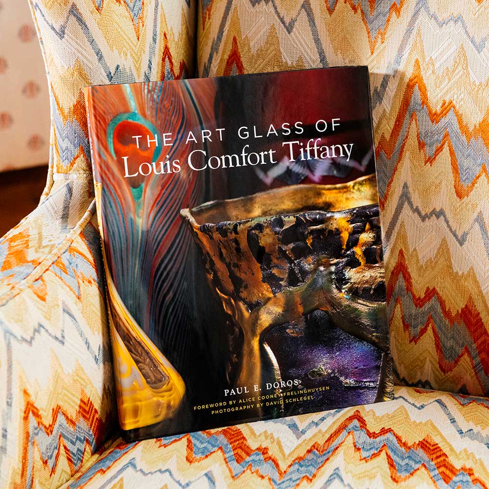 The Art Glass of Louis Comfort Tiffany rests on a chevron-patterned chair, its cover showcasing vibrant art glass.