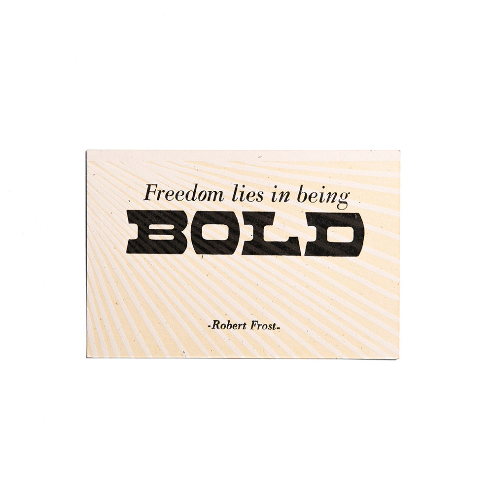 The Freedom Lies in Being Bold Postcard is a hand-printed letterpress card featuring Robert Frost’s quote, BOLD in large black letters, sunburst lines, and an antique wood and metal type-inspired design.