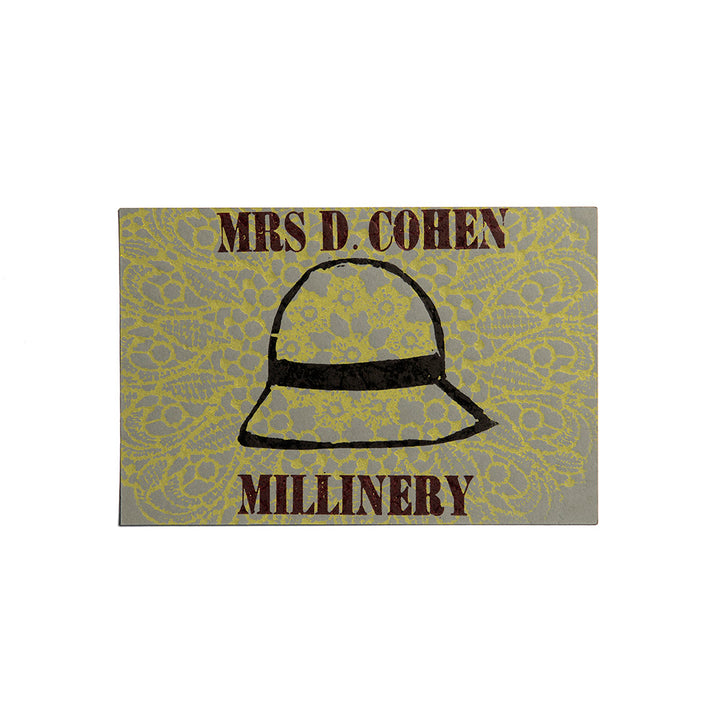 The Mrs. D Cohen Millinery Postcard features a yellow lace pattern, a central black hat outline, and bold brown "MRS. D. COHEN" above and "MILLINERY" below—artisan printed with antique wood and metal type.