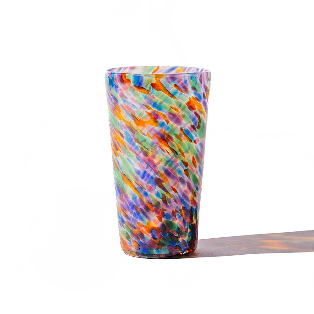 The Rainbow Frit Cup features a tall form and a multicolored speckled pattern in blue, orange, green, and purple, casting a vibrant shadow on a white background.