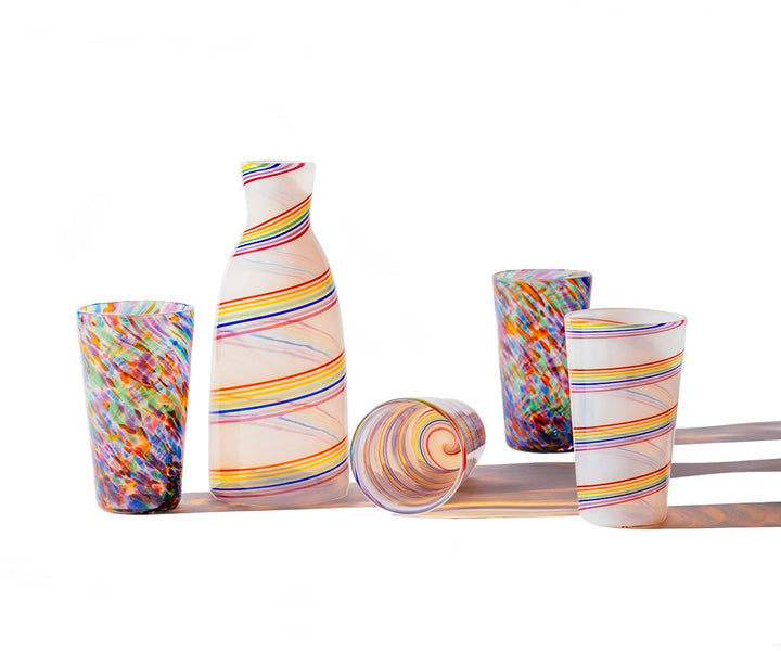 Five vibrant Rainbow Frit Cups feature swirling stripes and patterns, casting soft multicolored shadows on a white background. One tumbler is shown laid on its side.