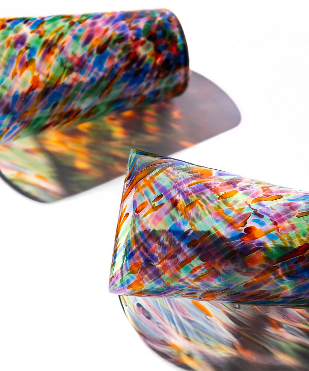 Two Rainbow Frit Cups rest on a white surface, casting vibrant, multicolored shadows. Each tumbler features a lively mix of red, blue, green, orange, and purple speckles.