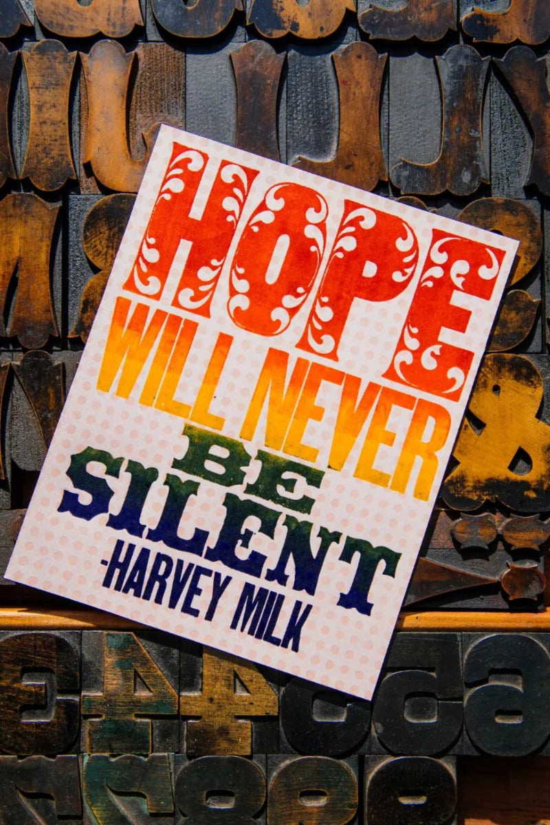 The Milk Quote Poster features bold, decorative text with the Harvey Milk quote "HOPE WILL NEVER BE SILENT" over wooden letterpress blocks and a subtle rainbow gradient.