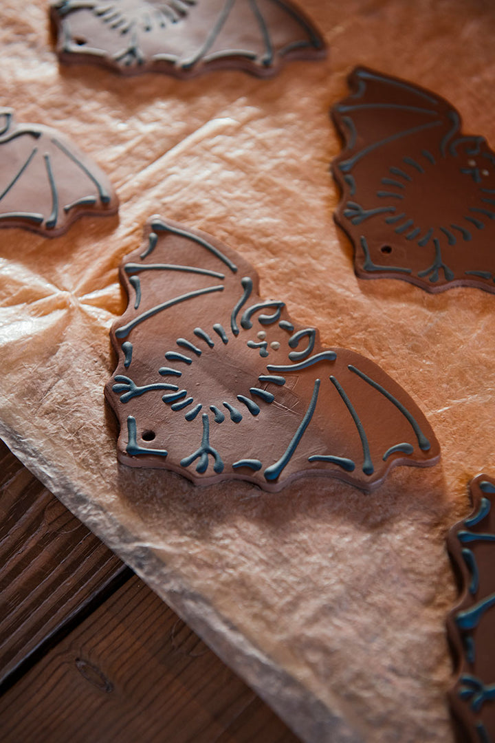Bat-shaped cookies with black icing rest on parchment atop wood, evoking the handcrafted Redware Bat Ornament from Greenfield Village pottery.