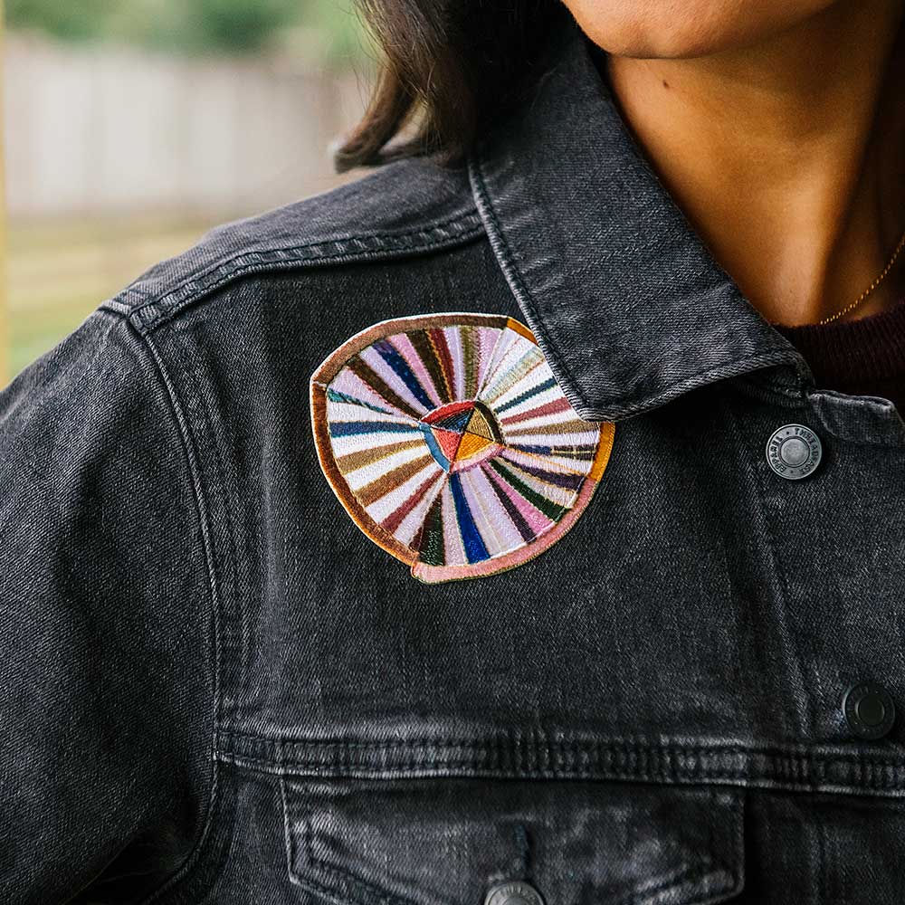 Wearing the Quilt Patches Denim Jacket—a black women's denim jacket with a large, colorful circular embroidered patch on the upper left—makes a bold statement at the Henry Ford Museum.