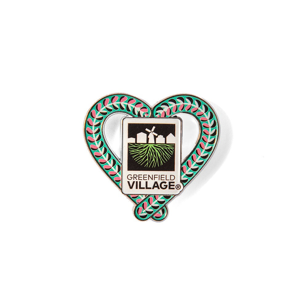 The Henry Ford® Greenfield Village Candy Cane Charm Magnet features a heart shape with a green and red leaf border, the Greenfield Village logo with three buildings, green fields, and “Greenfield Village”—a unique piece of memorabilia.