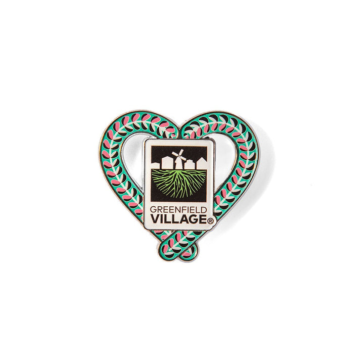 The Henry Ford® Greenfield Village Candy Cane Charm Magnet features a heart shape with a green and red leaf border, the Greenfield Village logo with three buildings, green fields, and “Greenfield Village”—a unique piece of memorabilia.