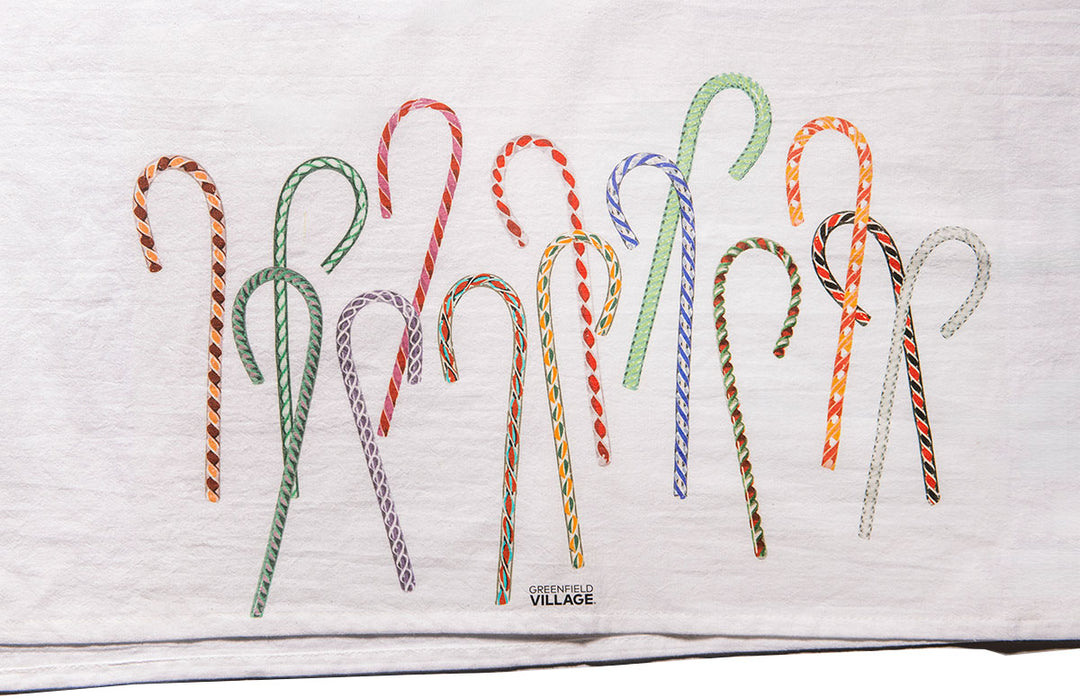 The Henry Ford® Greenfield Village Candy Cane Tea Towel is white, decorated with colorful hand-drawn candy canes. “Greenfield Village” appears subtly below, capturing the festive spirit of Henry Ford’s historic village.