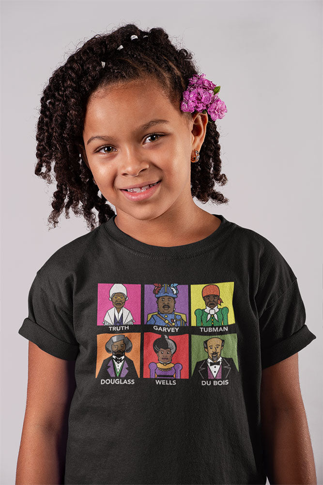 A smiling girl with curly hair and a purple flower wears the 'Freedom Fighters' AR Enhanced Youth T-Shirt, featuring illustrated portraits of Sojourner Truth, Marcus Garvey, Harriet Tubman, Frederick Douglass, Ida B. Wells, and W.E.B. Du Bois.