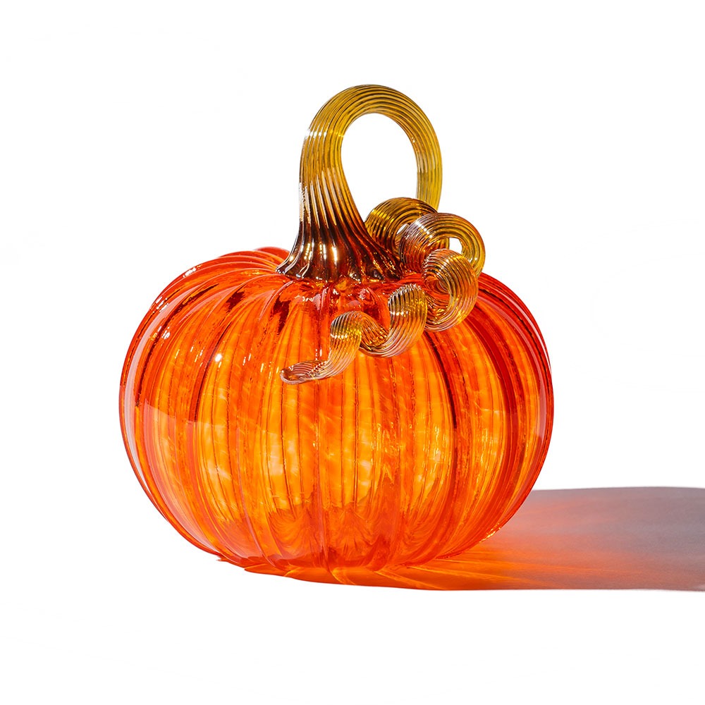 The Large Glass Pumpkin - Orange features vibrant hand-blown glass with a ribbed texture and curled yellow stem, casting a soft shadow—an ideal collectible for fans of Greenfield Village artistry.