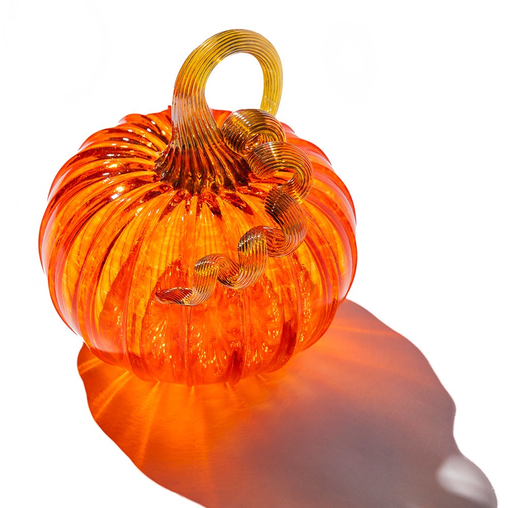 The Large Glass Pumpkin - Orange features hand-blown, bright orange glass with a ridged surface and a twisted, translucent yellow stem—ideal as a collectible keepsake and casting colorful shadows on any white background.