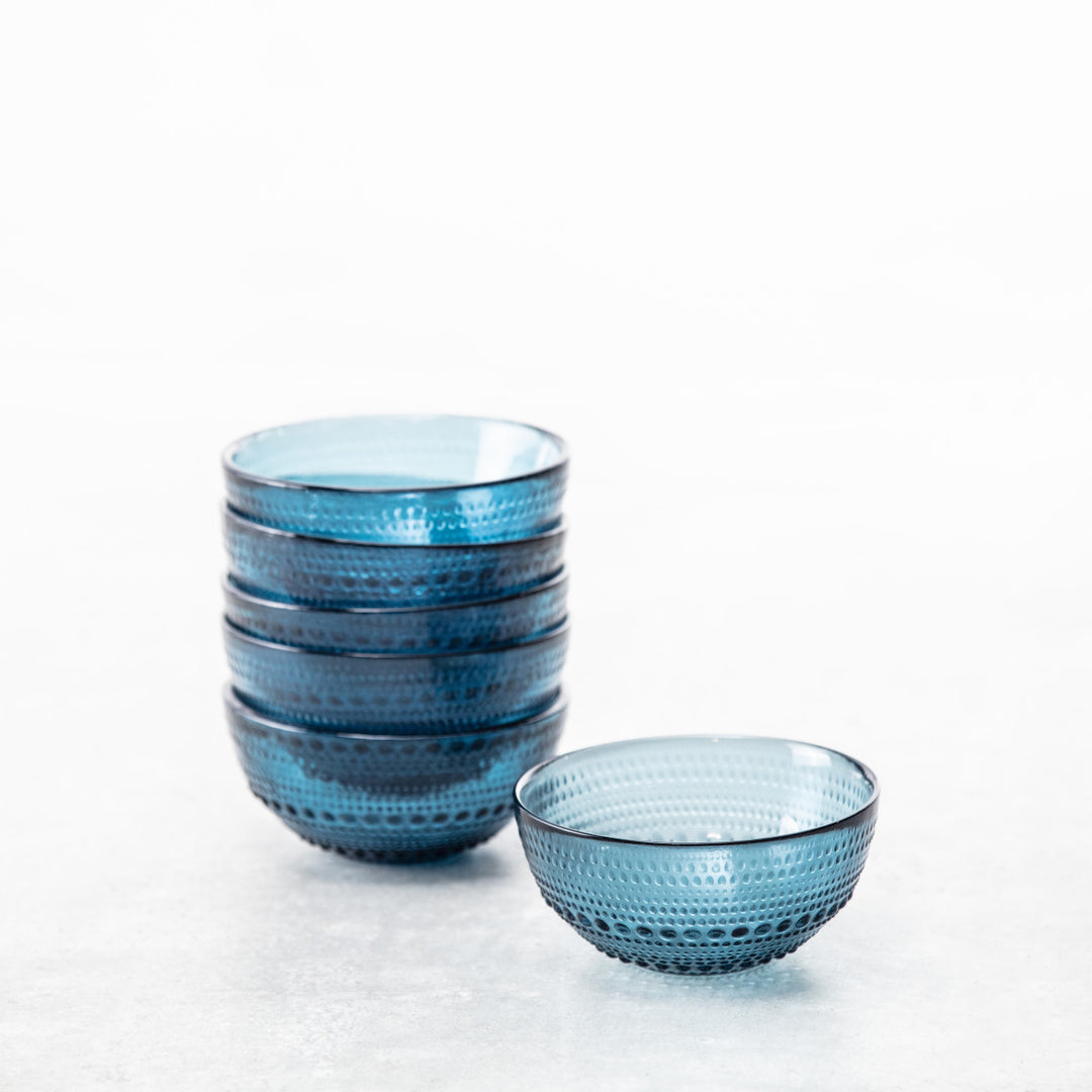 Six stacked Jupiter Cereal Bowls in Cornflower sit beside a matching bowl on a light surface with a white background, showcasing their beaded glassware design.