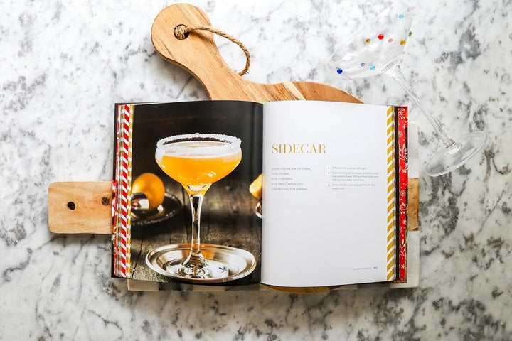 Holiday Cocktails: Over 100 Simple Cocktails to Celebrate the Season features a Sidecar recipe with a photo, set on marble with a cutting board and dotted martini glass—ideal inspiration for festive and holiday drinks.