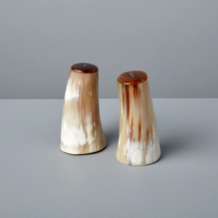 The Horn Salt & Pepper Shaker Set features two conical shakers with a smooth, marbled brown and cream finish, handmade and ethically crafted in Vietnam, displayed on a light gray surface against a plain gray background.