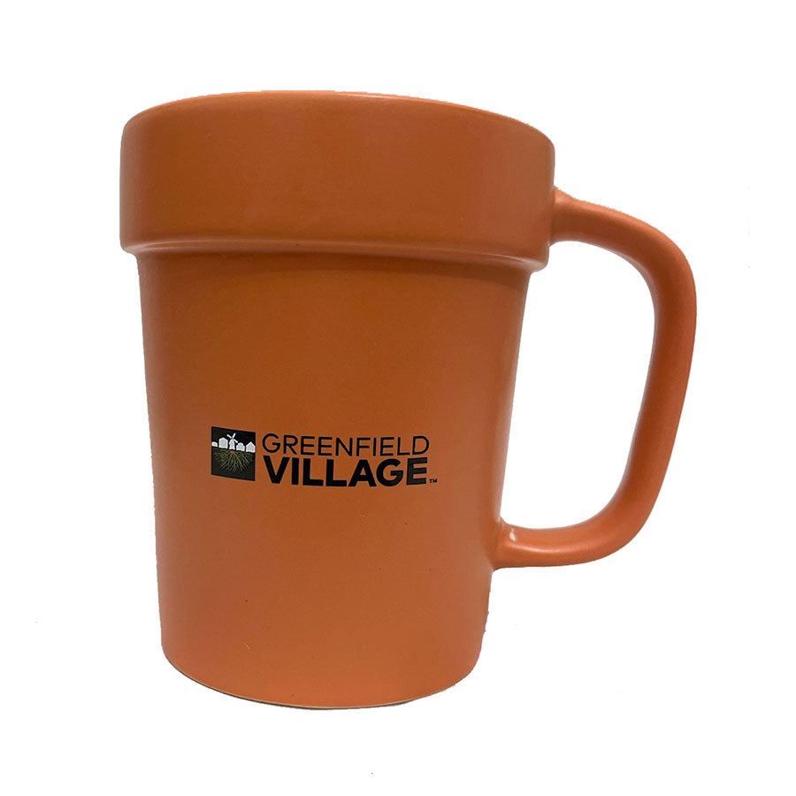 The Planter Mug is an orange ceramic coffee mug with a large handle, featuring the Greenfield Village logo and text in black on the front.