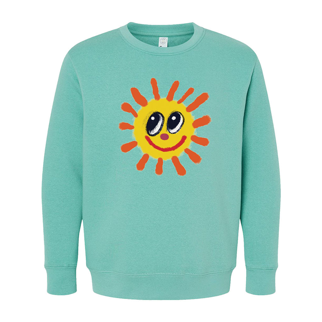 The Greenfield Village Happy Day Youth Sweatshirt is a light teal kids' top with a large cartoon yellow sun, orange rays, big black-and-white eyes, and a smiling red mouth by Humberto Cruz.