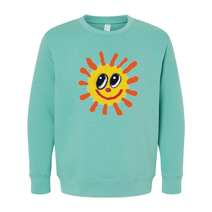 The Greenfield Village Happy Day Youth Sweatshirt is a light teal kids' top with a large cartoon yellow sun, orange rays, big black-and-white eyes, and a smiling red mouth by Humberto Cruz.