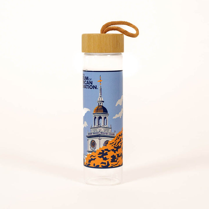 The Henry Ford Museum Building Glass Water Bottle features clear glass, a bamboo lid, tan carrying loop, and an illustrated domed building with trees and "Museum of American Innovation" text.