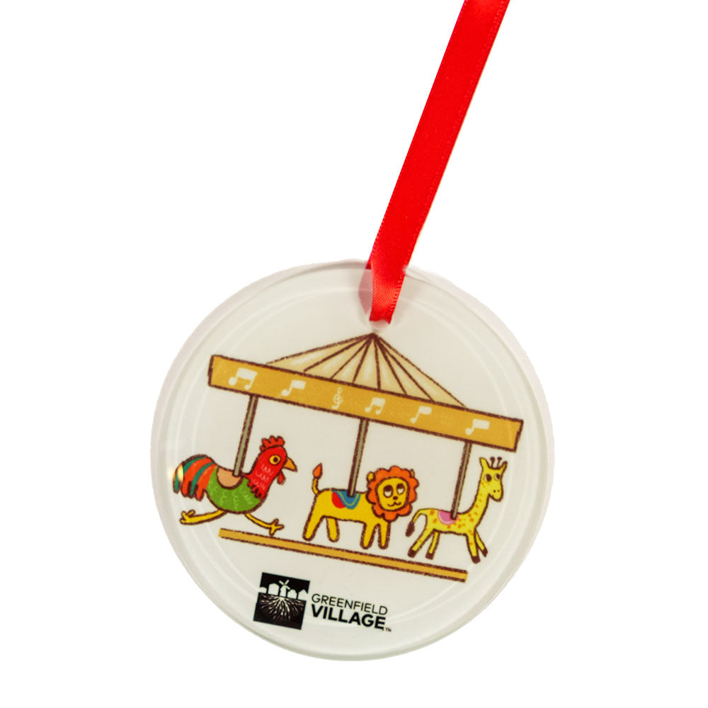 The Greenfield Village Carousel Ornament is a round ornament with a red ribbon, featuring Humberto Cruz’s artwork of a carousel (rooster, lion, giraffe), musical notes at the top, and the Greenfield Village logo at the bottom.