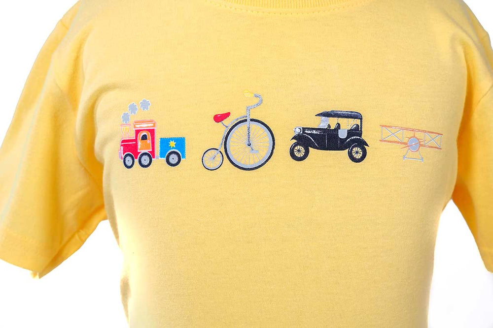 The Greenfield Village Icons Toddler T-Shirt is yellow and features Humberto Cruz-inspired embroidered images—a red train, unicycle, vintage black car, and yellow biplane—arranged in a playful row across the chest.