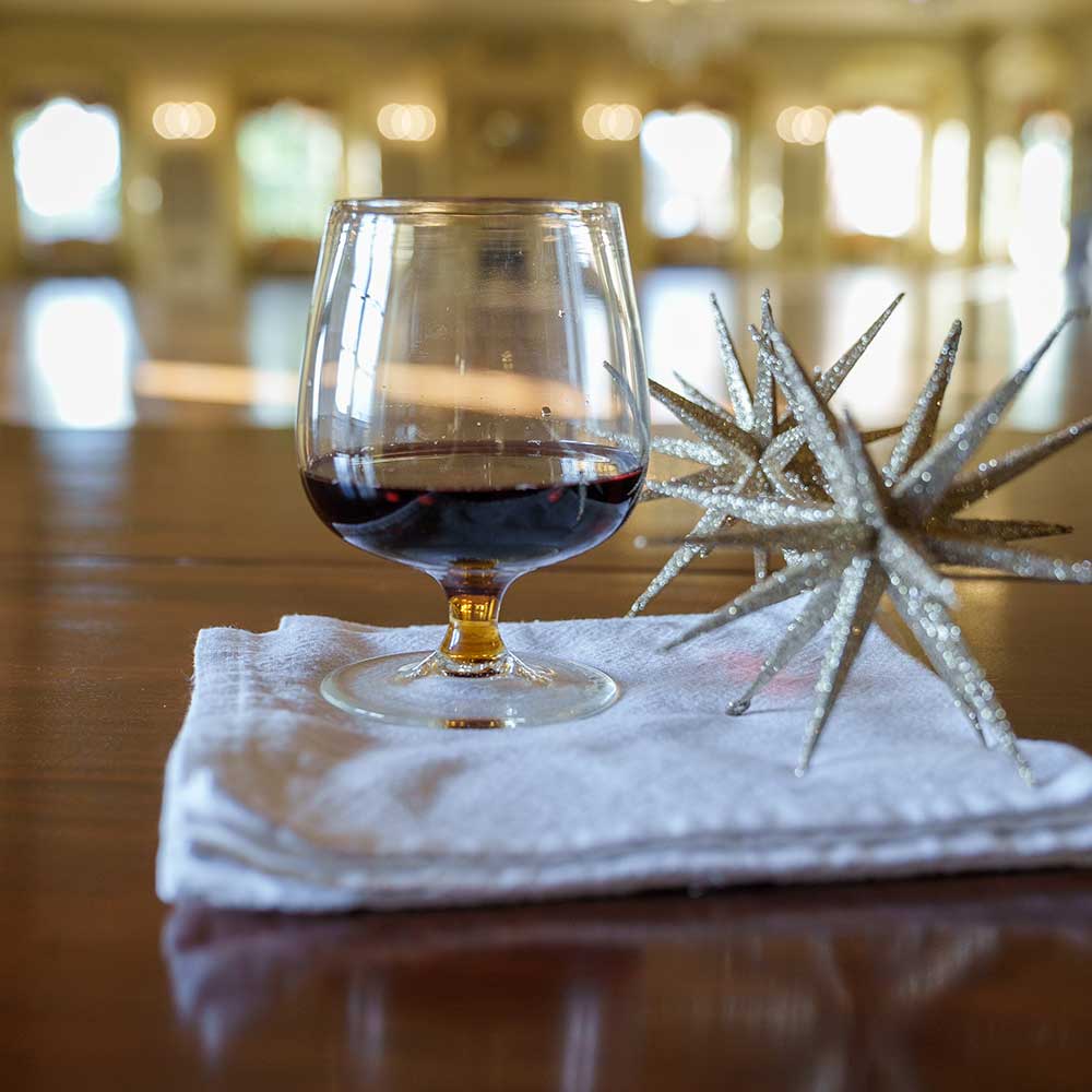 A Mixology Short-Stemmed Red Wine Glass rests on a folded white napkin atop a wooden table beside two decorative silver star ornaments, with a softly blurred background bathed in warm natural light.