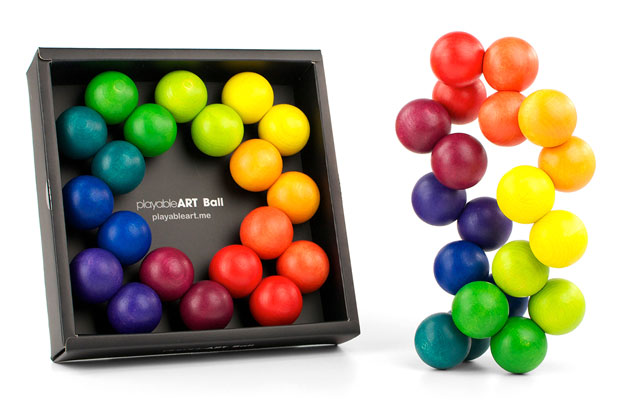 The Playable Art Ball is a set of colorful wooden balls arranged in a circle inside a black box on the left and displayed in a wavy vertical form on the right, featuring a rainbow gradient for creative desk play.
