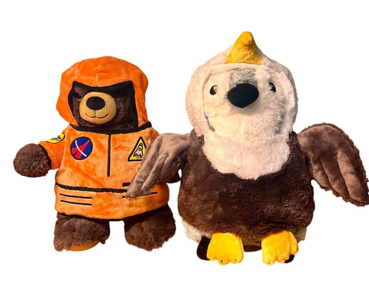 Two plush toys on a white background: one is a bear in an orange astronaut suit, and the other is wearing the Plush Eagle Outfit with brown wings, a yellow beak, and soft white and brown feathers.