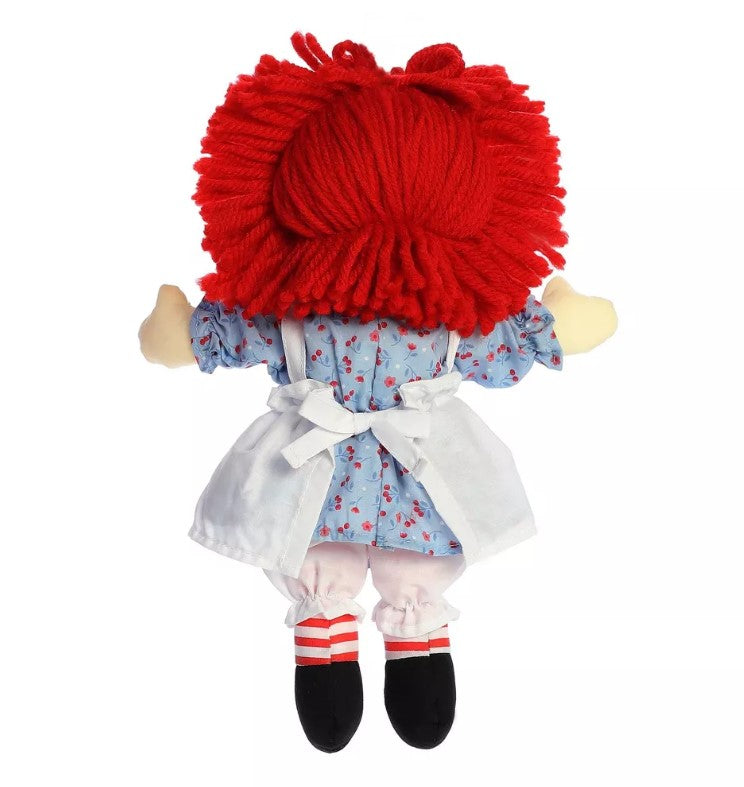 Raggedy Ann doll with bright red yarn hair, blue floral dress, white apron and bloomers, black shoes, and red-and-white striped socks, pictured from the back.