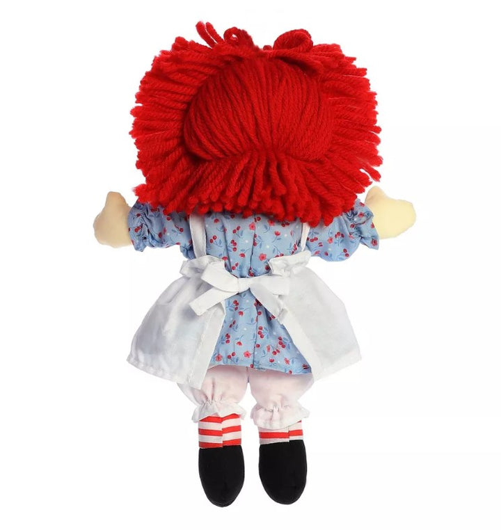 Raggedy Ann doll with bright red yarn hair, blue floral dress, white apron and bloomers, black shoes, and red-and-white striped socks, pictured from the back.