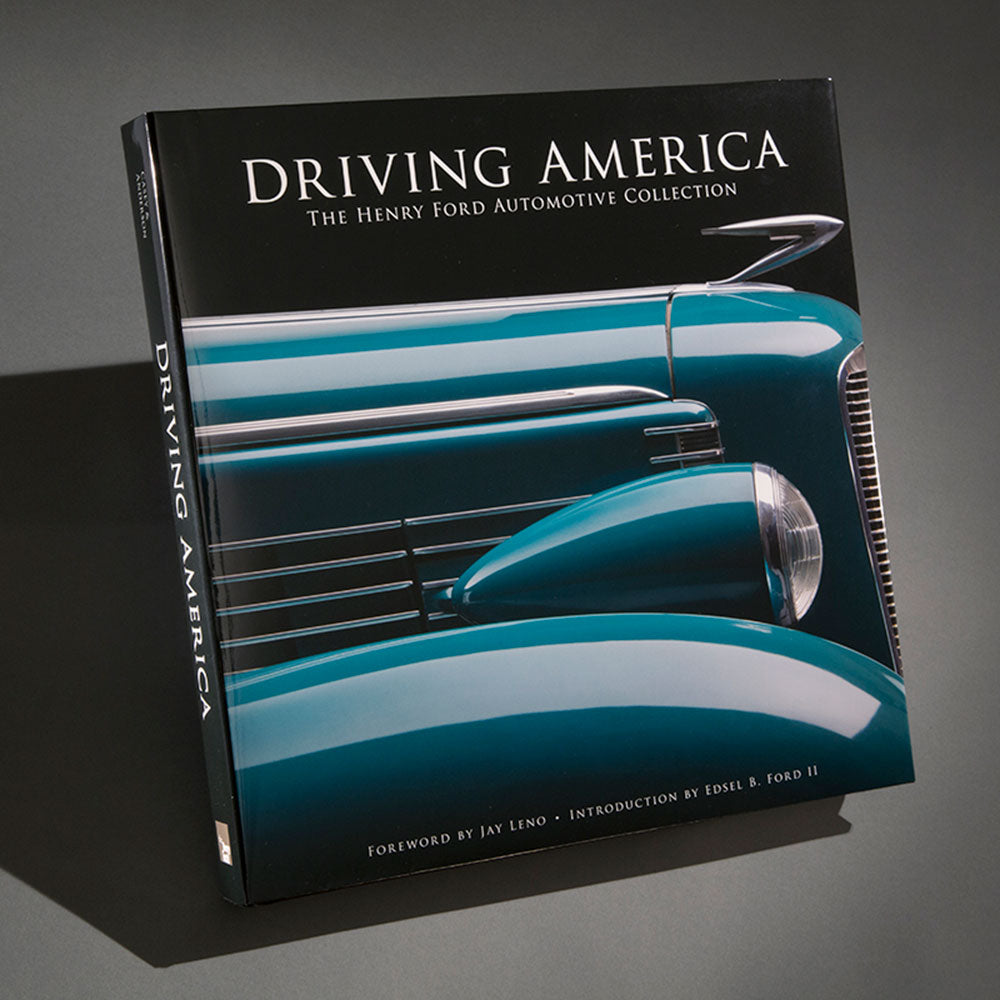 The hardcover edition of Driving America: The Henry Ford Automotive Collection features a close-up of a classic blue vintage car on its cover, angled against a gray background.