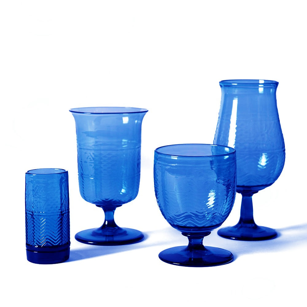 A steel blue American Heritage Molded Wine Goblet is arranged on a white background. This handmade glass features a unique textured pattern and distinct form, standing out among other blue glassware in the collection.