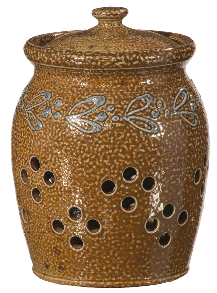 The Stoneware Garlic Keeper is a brown ceramic jar with a fitted lid, blue and white leaf design near the top, and multiple round ventilation holes in the body to keep garlic fresh.