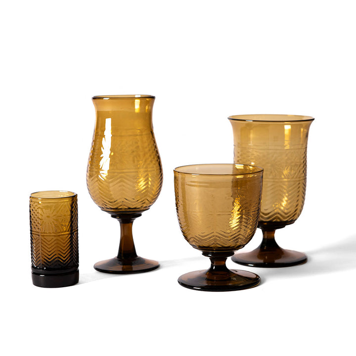 An American Heritage Molded Water Goblet - Tea is shown on a white background, featuring amber-hued handmade glass with an embossed zigzag and floral design.