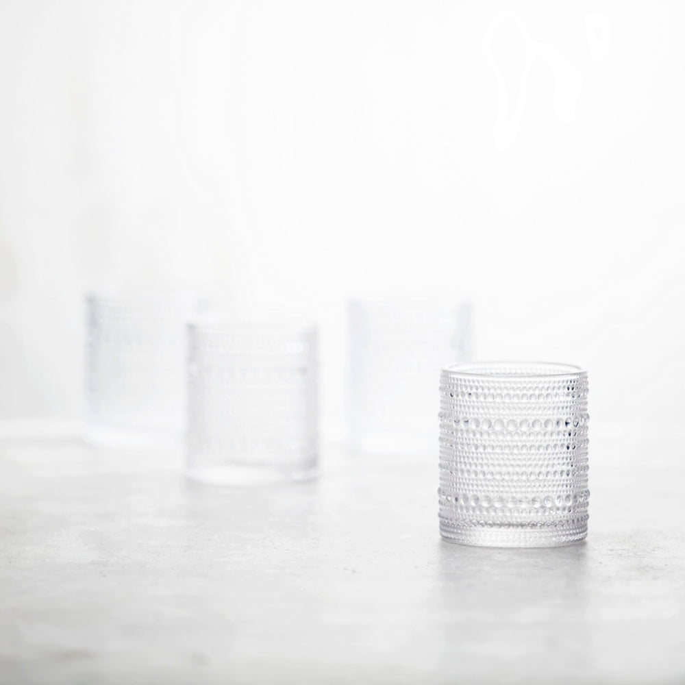 Three clear Jupiter Old Fashioned Glasses are arranged on a softly blurred surface; one elegant glass is in sharp focus in the foreground, while the other two appear out of focus in the background.