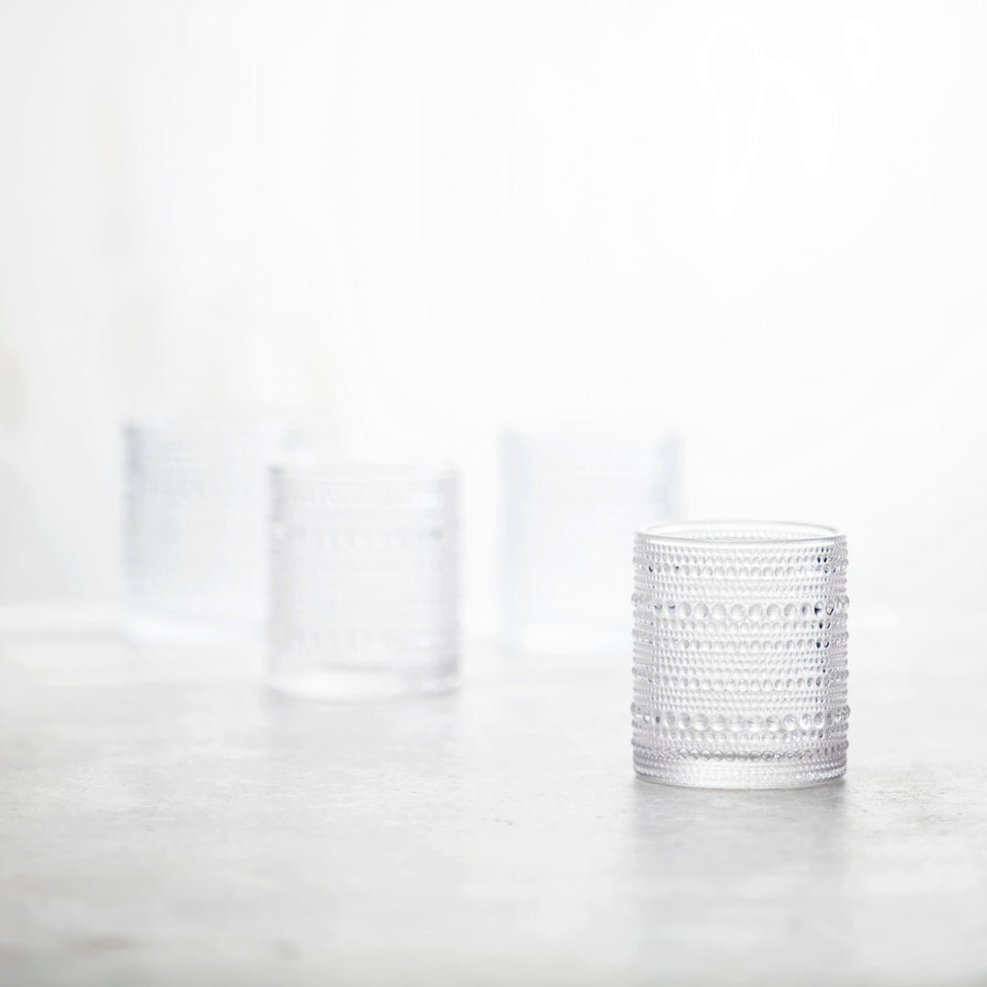 Three clear Jupiter Old Fashioned Glasses are arranged on a softly blurred surface; one elegant glass is in sharp focus in the foreground, while the other two appear out of focus in the background.