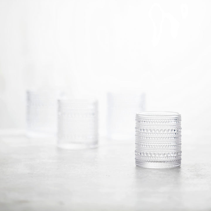 Three clear Jupiter Old Fashioned Glasses are arranged on a softly blurred surface; one elegant glass is in sharp focus in the foreground, while the other two appear out of focus in the background.