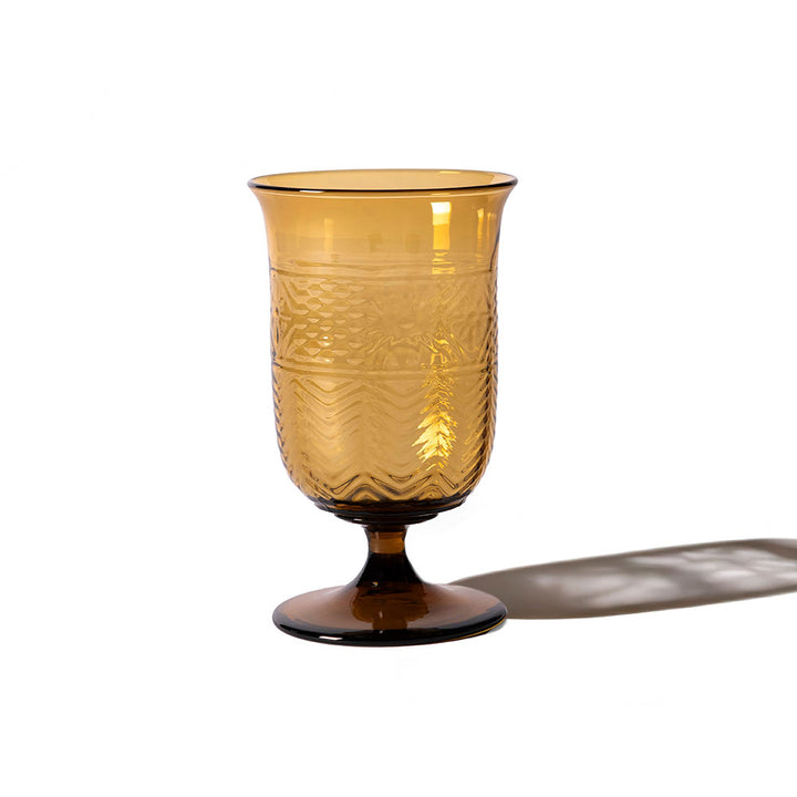 The American Heritage Molded Water Goblet - Tea is a vintage-style amber glass featuring decorative textured patterns, a wide rim, and a short stem, casting a soft shadow on a white background.