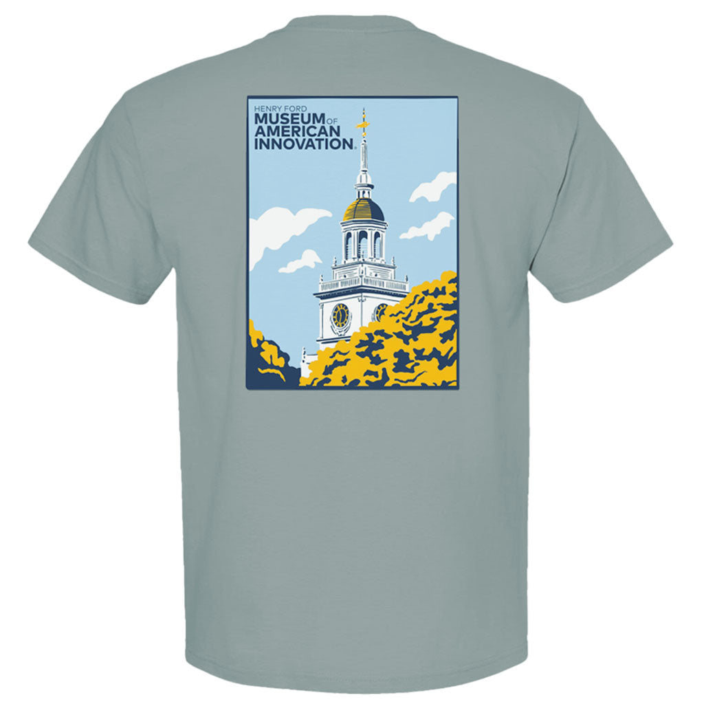 The Henry Ford Museum Clocktower T-Shirt is light gray, features a white clock tower with a gold top and clouds partially hidden by trees, plus “Henry Ford Museum of American Innovation” text. Made from soft organic cotton.